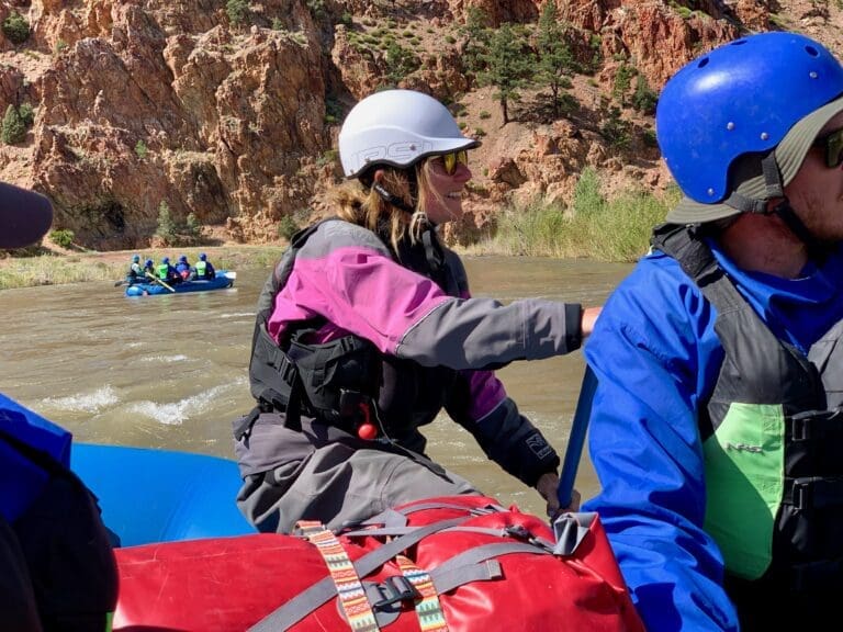 Two people rafting in a boat with another boat in the background.