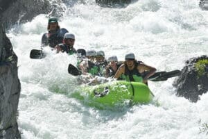 People on a rafting boat in the middle of class four rapids getting splashed by water.