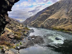 Deep river canyon with water flowing through it and tall mountain peaks surrounding it.