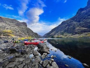 A couple of boats on the shore of a river. Calm river water with reflection of mountain peaks