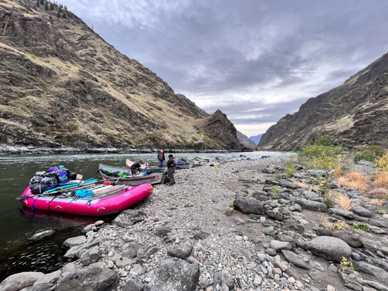 People standing on shore next to one inflatable rafting boat and a few metal fishing boats loaded with gear.